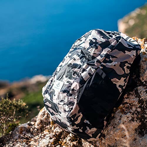 Camouflage backpack on rocky terrain by the sea.