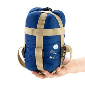 Compact blue sleeping bag in hand with beige straps.