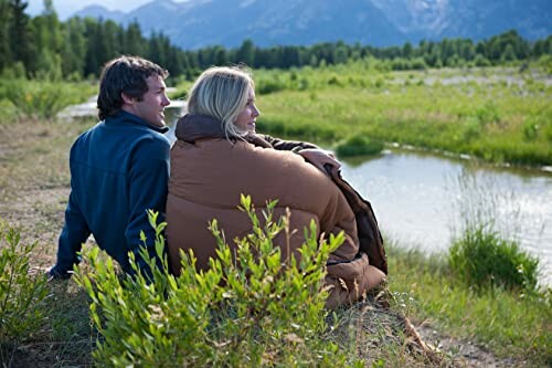 Couple sitting by a river with mountains in the background.