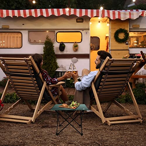 Couple sitting in deck chairs outside a camper, toasting with drinks.