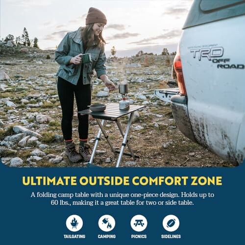 Person using a folding camp table near a vehicle in a rocky outdoor setting.