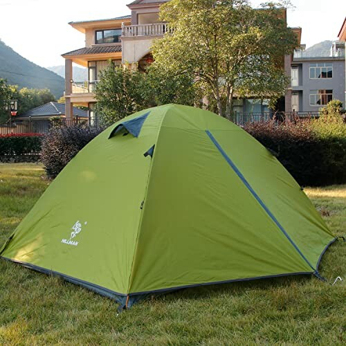 Green tent set up on grass near houses and trees.