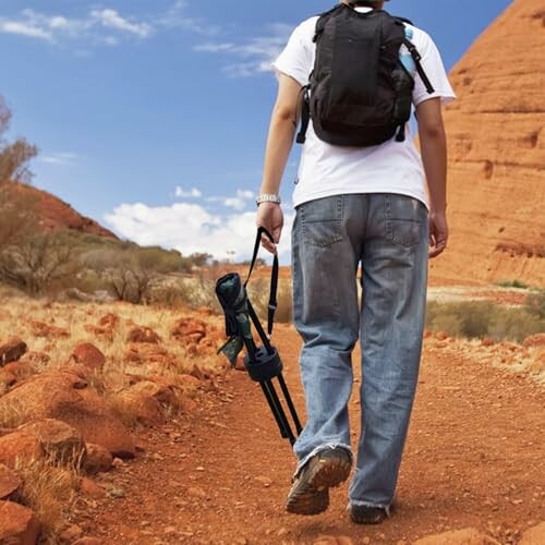 A person hiking on a desert trail carrying a tripod