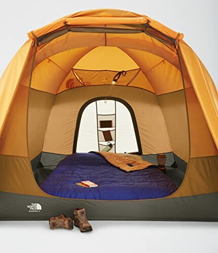 Interior of an orange camping tent with a sleeping bag and boots.