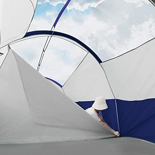 Person adjusting a tent interior with sky view.