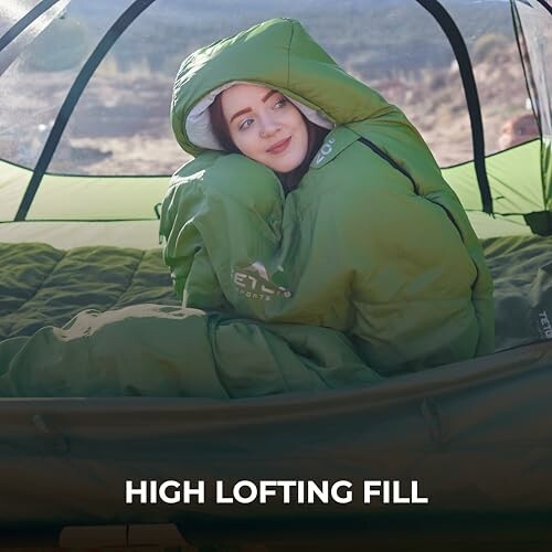 Woman in a green sleeping bag inside a tent, smiling.