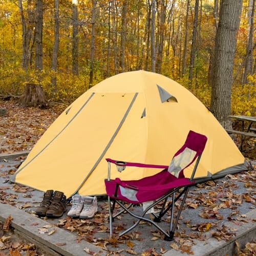 Yellow tent with camping chair and shoes in autumn forest.